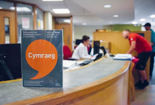 Poster Iaith Gwaith ar ddesg y dderbynfa