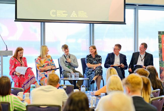Panel o siaradwyr yn eistedd mewn cynhadledd
